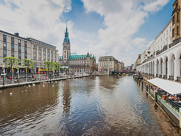 Blick über die Alsterarkaden in Hamburg mit Wasser, Cafés und historischem Rathaus im Hintergrund